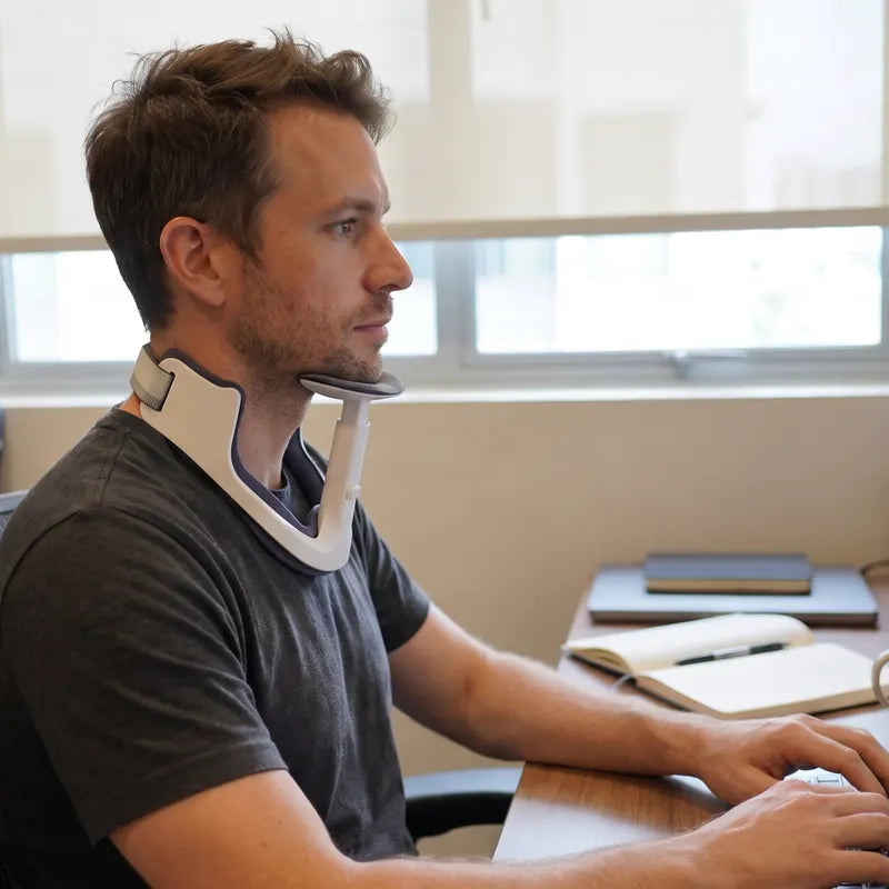A man typing at a desk wearing NAPE: his chin rests on the padded chin rest and his eyes are level with the monitor