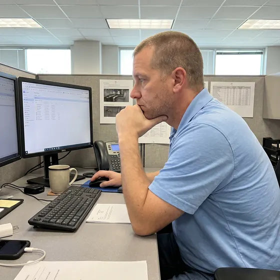 A man at a cubicle desk reading his screen with his fist under his chin