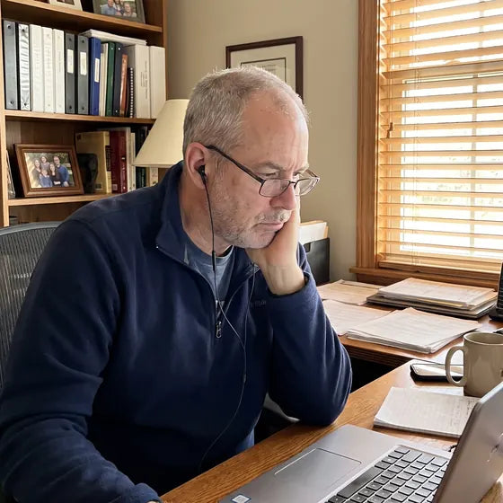 A man at a home desk with his cheek resting in the palm of his hand